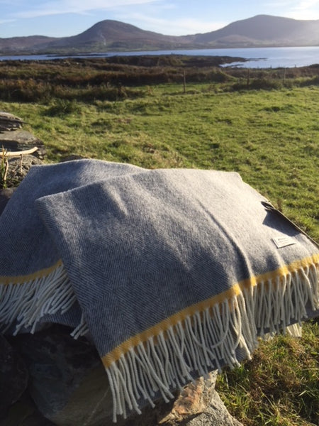 Woven from the finest merino lambswool in a subtle diamond pattern, this uniform grey baby blanket has a pop of yellow at each end.